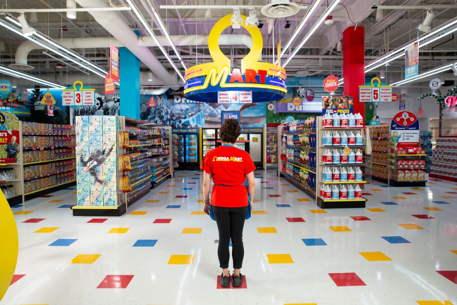 An Omega Mart employee in a red uniform standing beneath a glowing Omega Mart sign, facing down a grocery aisle stocked with surreal, brightly colored fake products