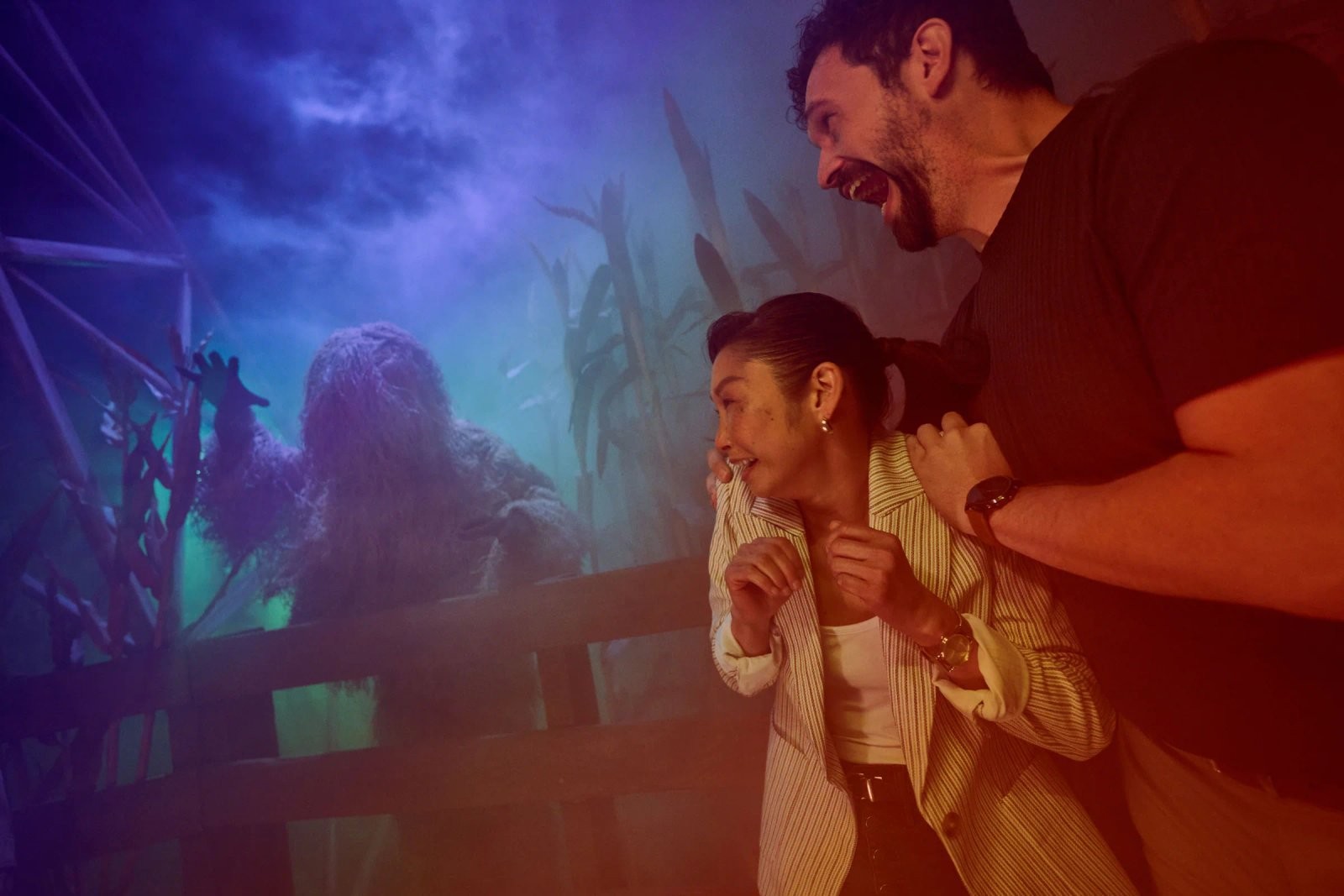 Two startled guests react as a costumed werewolf-like creature looms behind a cornfield-themed set inside Universal Horror Unleashed