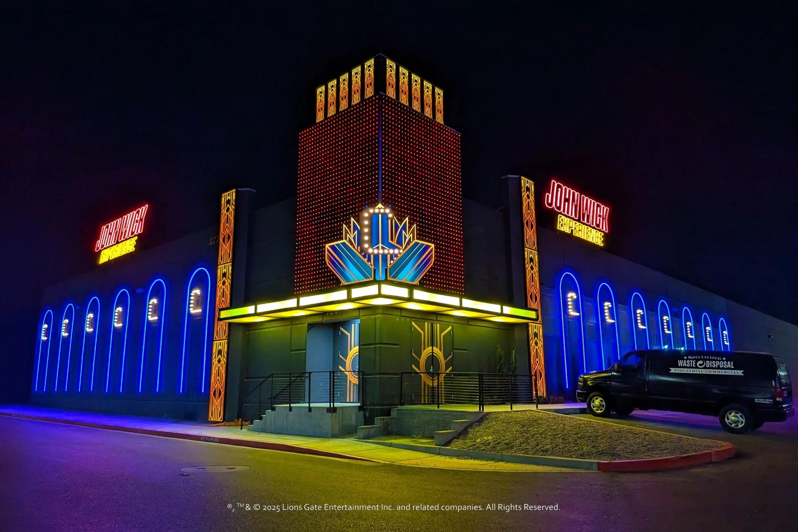 The John Wick Experience's Art Deco-style exterior facade at night, lit in red, gold, and blue neon with a marquee entrance
