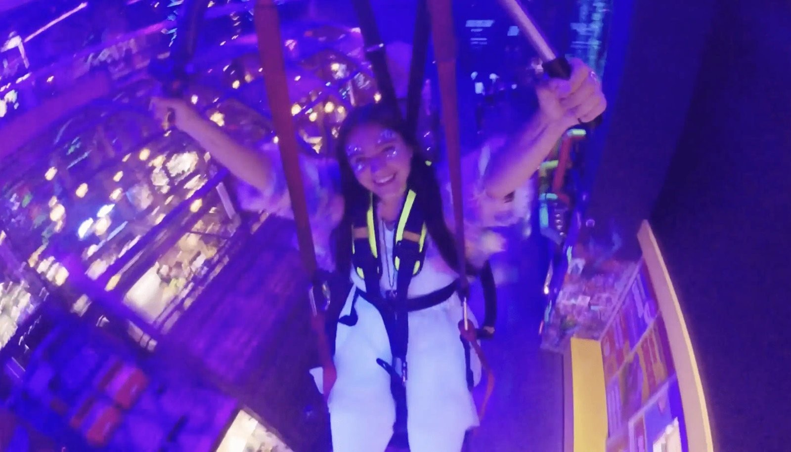 A rider's point-of-view selfie-cam shot mid-flight on Haley's Comet, harnessed and smiling above The Spine's purple-lit main hall