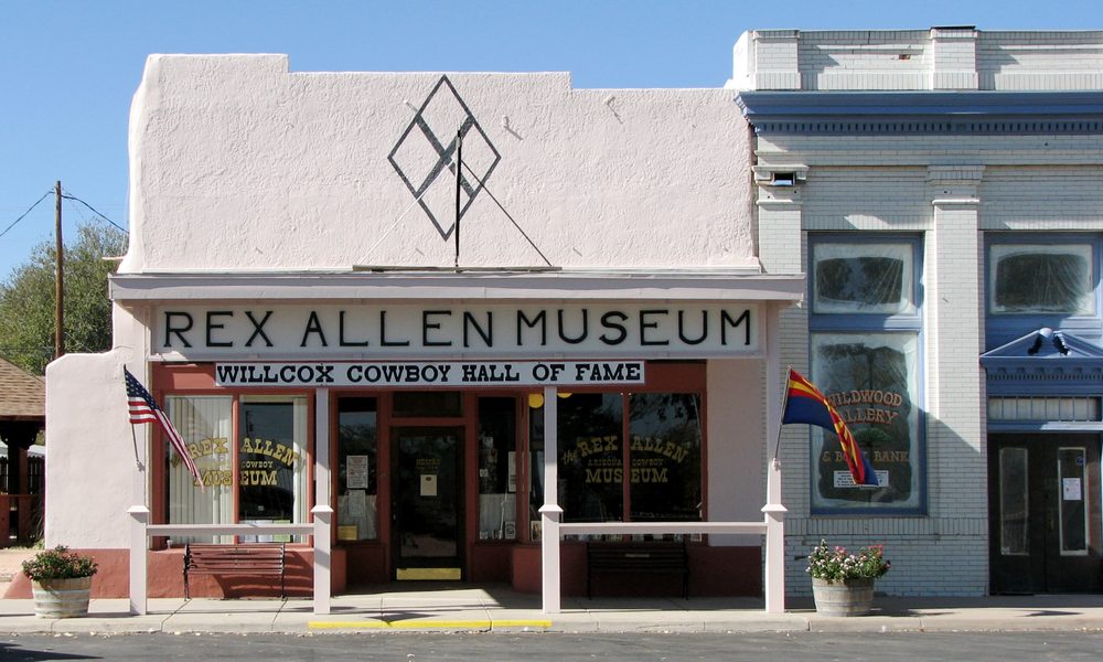 The pink storefront of the Rex Allen Museum and Willcox Cowboy Hall of Fame in Willcox, Arizona, with an American flag and an Arizona state flag out front