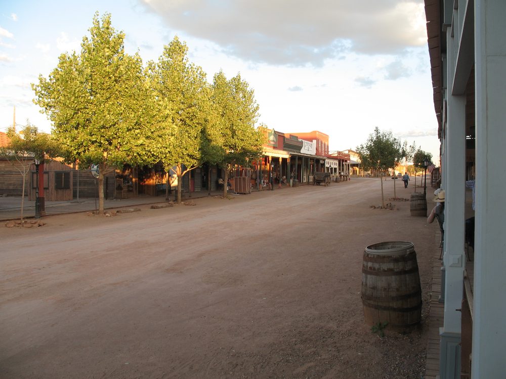 A dirt street in Tombstone, Arizona lined with historic Old West storefronts and wooden barrels, lit by late-afternoon sun