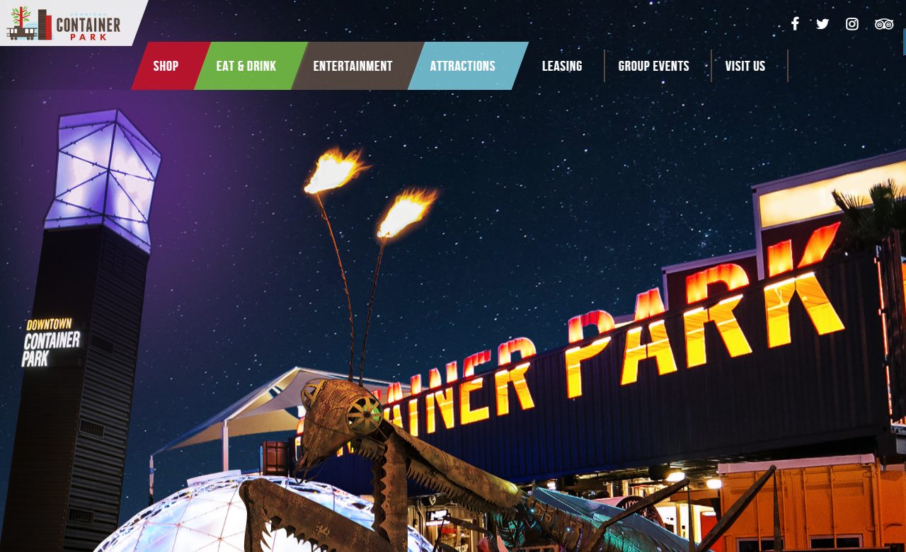 Downtown Container Park's entrance at night, showing its giant metal praying mantis sculpture shooting real fire from its antennae above the container-built storefronts