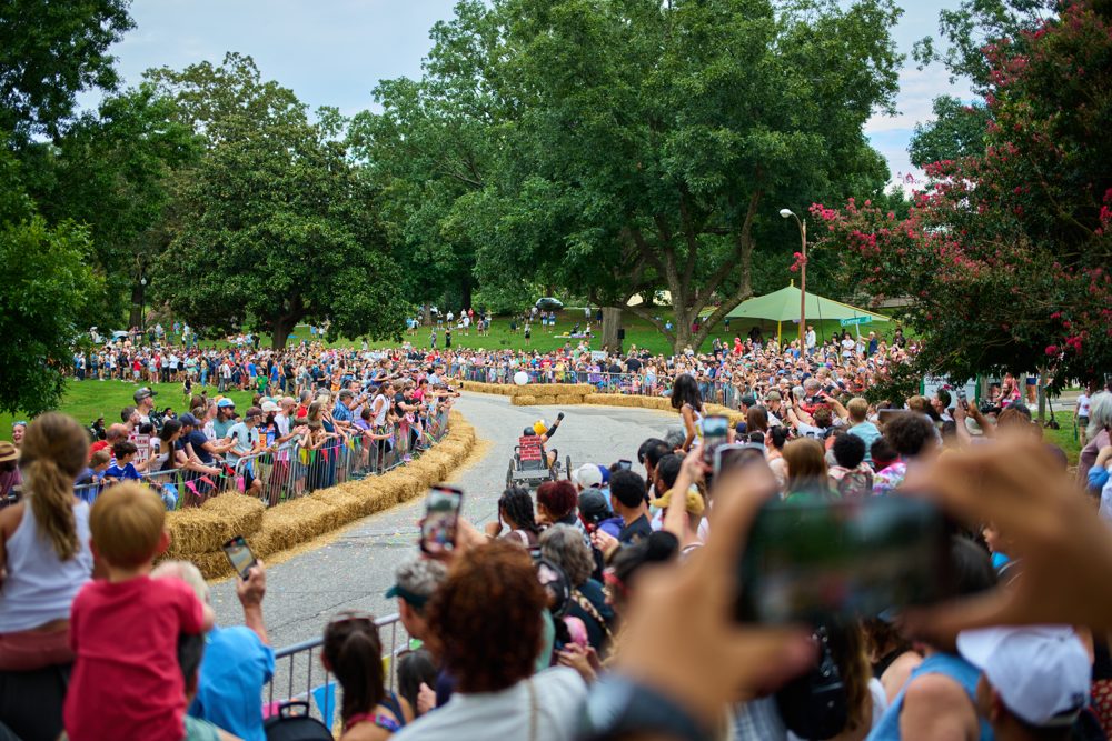 The downhill race course at a past Kirby Derby, lined with hay bales and packed with a cheering crowd on the hillside at Dorothea Dix Park