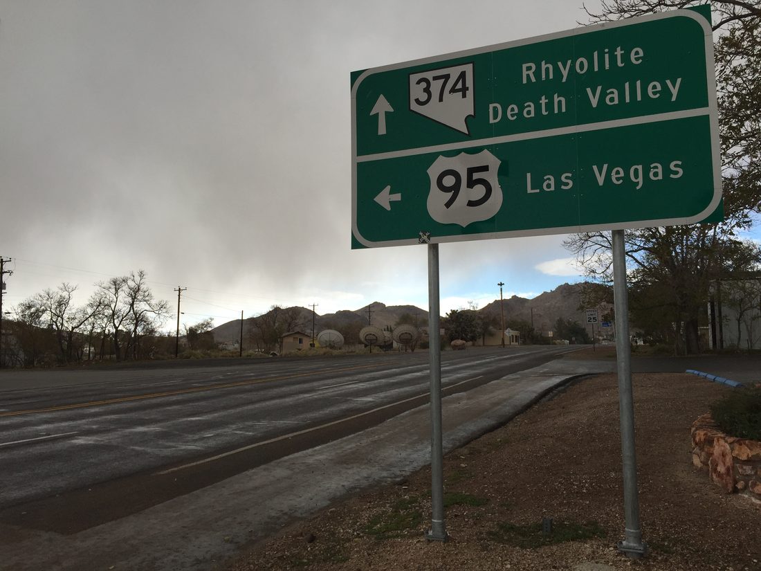 A green highway sign in Beatty, Nevada showing State Route 374 to Rhyolite and Death Valley straight ahead, and US Route 95 to Las Vegas to the left