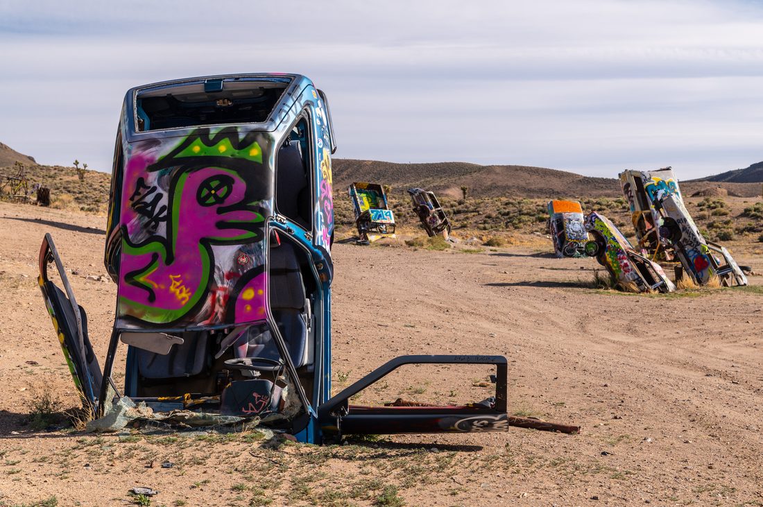 A vertically buried, graffiti-painted van and a row of similarly painted cars standing on end in the desert at the International Car Forest of the Last Church near Goldfield, Nevada