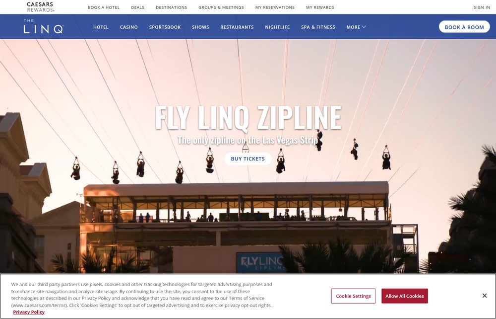 Riders soaring on the Fly LINQ zipline over The LINQ Promenade at sunset, launching from a multi-story tower
