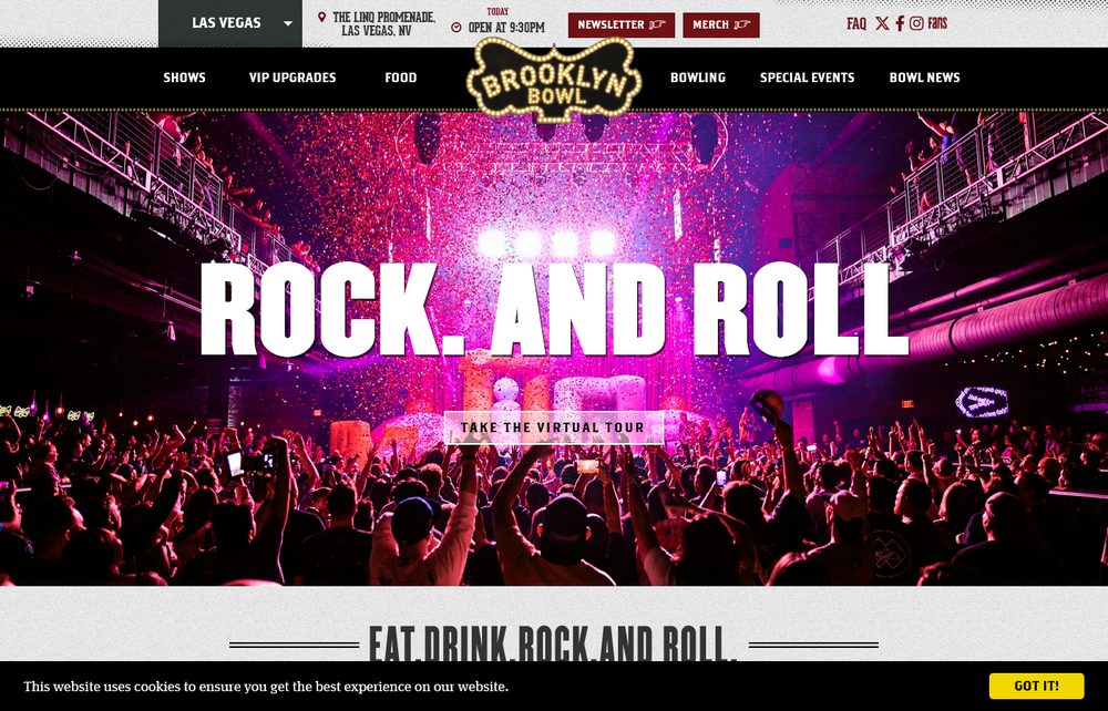 A packed crowd at Brooklyn Bowl Las Vegas with hands raised under confetti and pink and purple concert lighting
