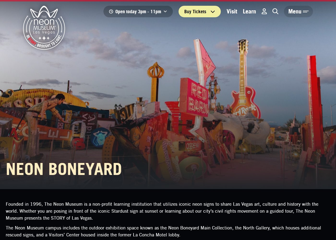 The Neon Museum's own webpage for the Neon Boneyard, showing a wide dusk view of the outdoor sign collection including a large fiberglass hand sculpture, a giant Hard Rock Cafe guitar, and a red star sign