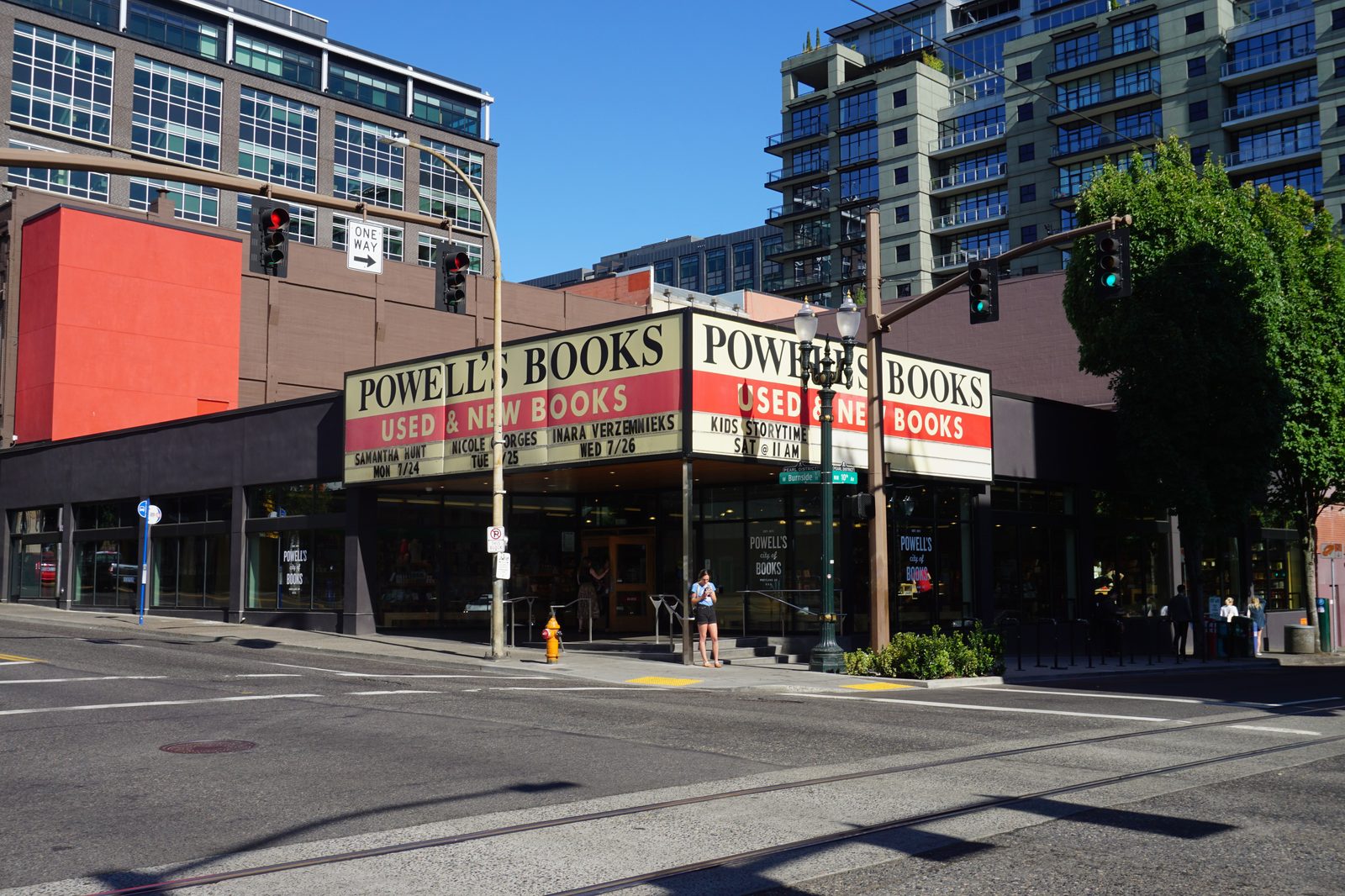The exterior of Powell's City of Books, a large independent bookstore taking up a full city block in the Pearl District of Portland, Oregon, with a red-and-cream sign reading POWELL'S BOOKS USED & NEW BOOKS