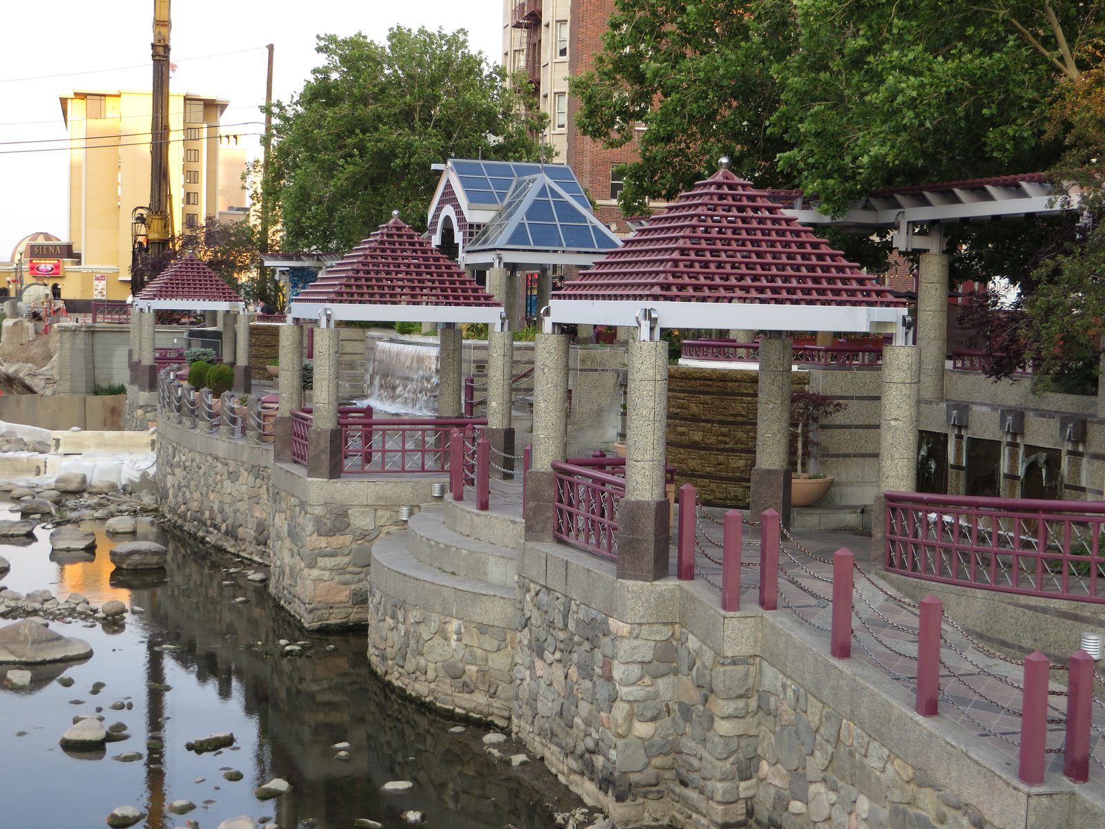 A sunset view of the Riverwalk District along the Truckee River in downtown Reno, Nevada, showing a landscaped riverbank walking path lined with rock walls and flowers