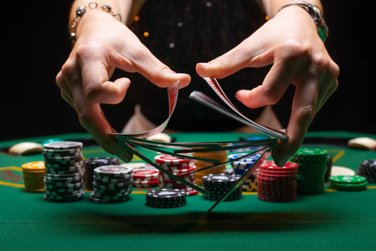 Close-up photo from Caesars.com of hands fanning playing cards over stacked casino chips on a green felt table