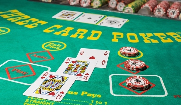 A real Three Card Poker table on green felt, showing the Ante, Play, and Pair Plus betting spots with a dealt hand of cards and stacked casino chips