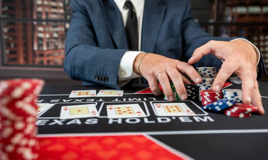 A real photo of a dealer at a branded Ultimate Texas Hold'em table, collecting chips next to dealt hole cards on the felt